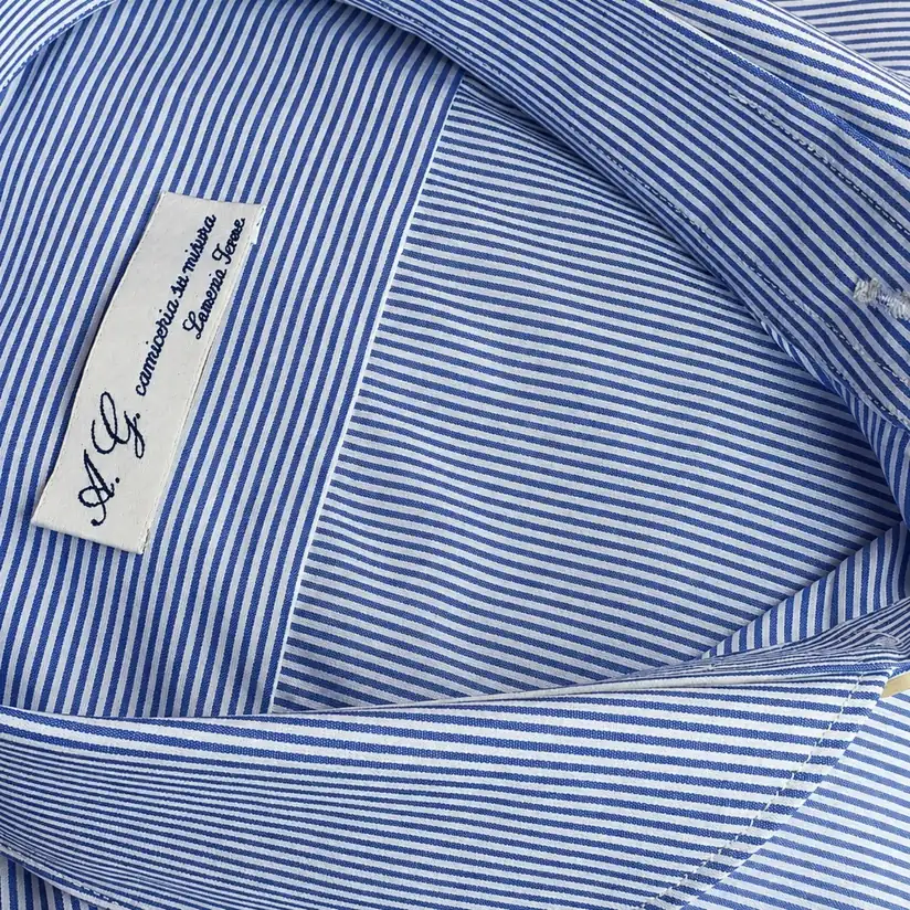 Dettaglio del collo di una camicia a righe blu e bianche con etichetta della camiceria Antonio Gigliotti.